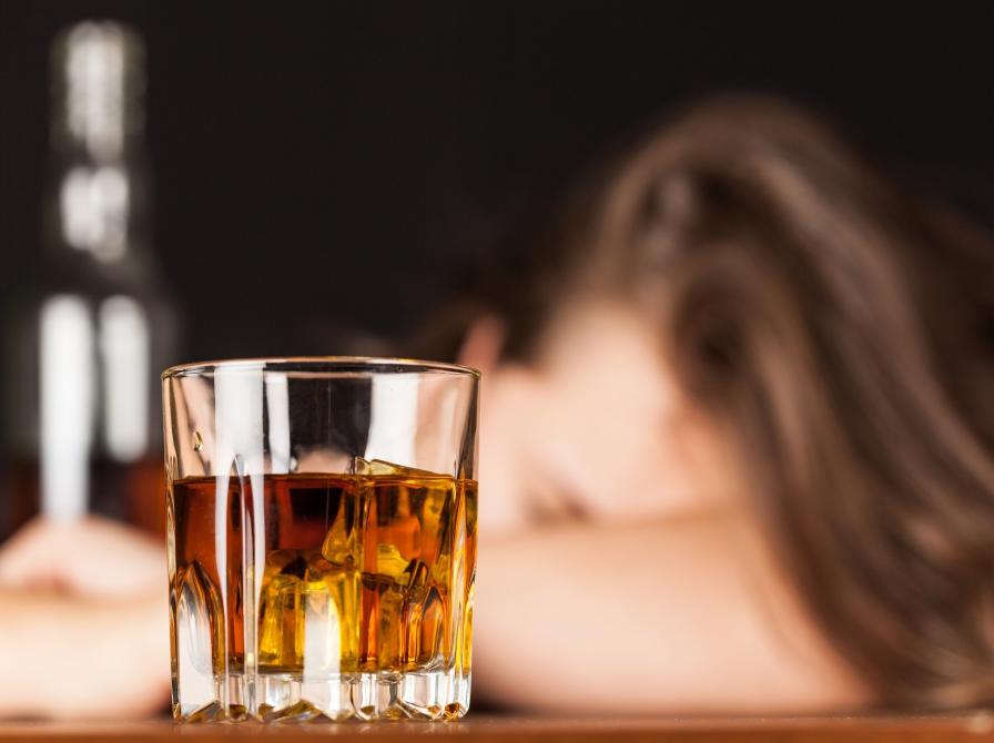 Et glas med alkohol og en kvinde der sover i baggrunden